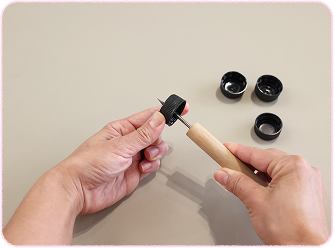 黒いペットボトルのキャップの中心に、キリで穴をあける。