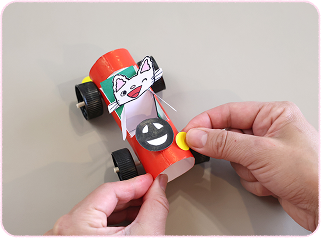 いすを置き、ハンドルとライトを飾りつけて、完成。前後に動かすとタイヤがまわる！